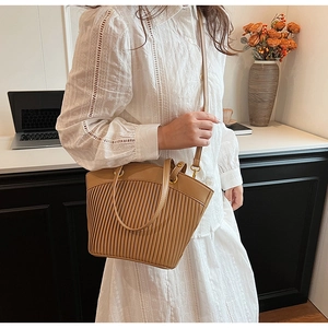 Lifestyle shot of a khaki pleated straw tote bag worn by a model in a bright room