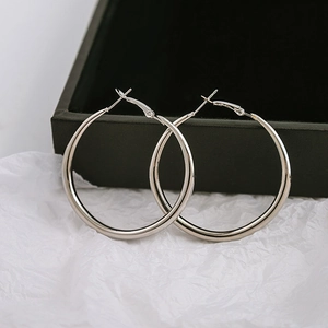 Close-up of polished silver hoop earrings on a textured paper and black box