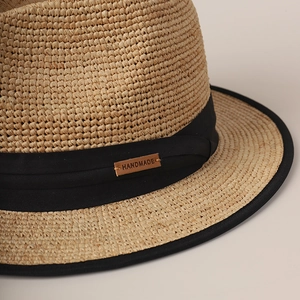 Detail of a handmade beige straw hat with a black ribbon and brown leather label