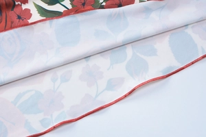 Detailed close-up of summer dress fabric showing red flower print and fine red hem stitching