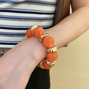 Close-up of bohemian chunky orange acrylic beads and gold ring spacers on a model wrist
