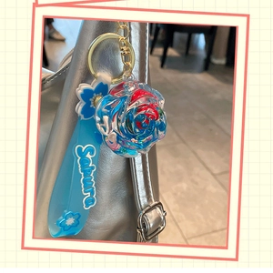 Blue sakura flower keychain with silicone strap hanging on a stylish silver leather bag