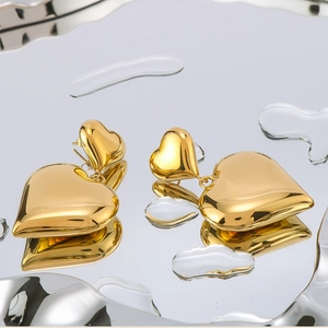 Polished 18K gold-plated double heart drop earrings on a reflective water drop background