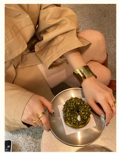 Close-up of polished gold wide cuff bracelet and chunky rings on a chic social scene