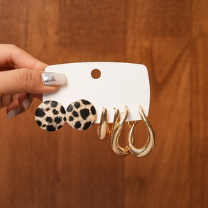 Detail of hand holding 6-piece earring set featuring leopard print studs and gold teardrop hoops