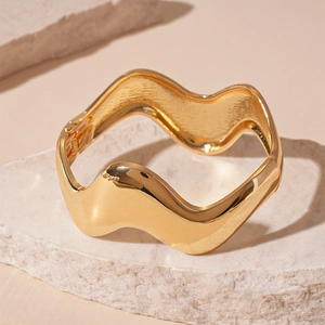 Detailed macro view of a golden wavy bangle resting on a natural stone minimalist pedestal