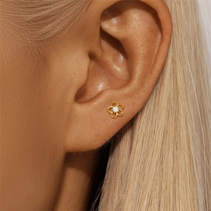 Detailed view of a gold flower stud earring with a central zircon worn on the ear