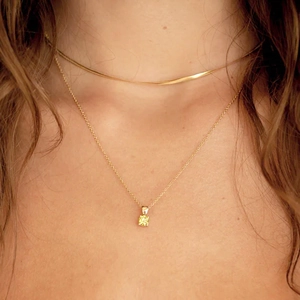 Close-up of layered gold snake chain and yellow square gemstone pendant on model's neck