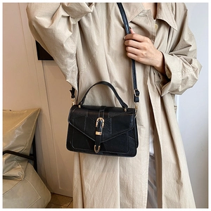 Close-up of black leather crossbody bag featuring a stylish golden U-shaped metal buckle
