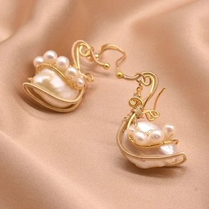 Golden swan-shaped baroque pearl earrings on champagne silk background