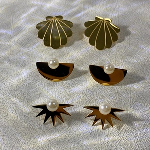 Three pairs of elegant 18k gold titanium steel earrings with pearls on woven background