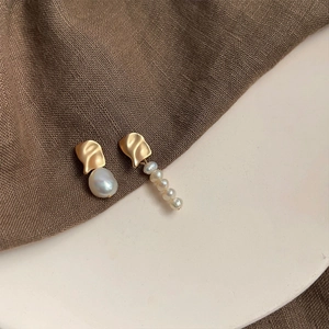 Macro detail of asymmetric baroque pearl earrings with matte gold metal finish
