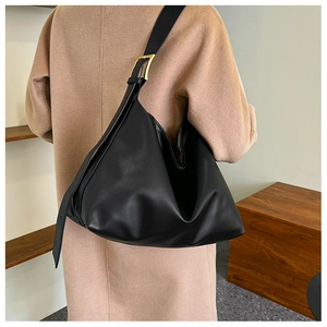 Detail of large black leather tote bag with gold buckle styled on a camel coat