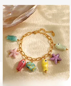Detail of gold marine charm bracelet with colorful ceramic fish and starfish on sand