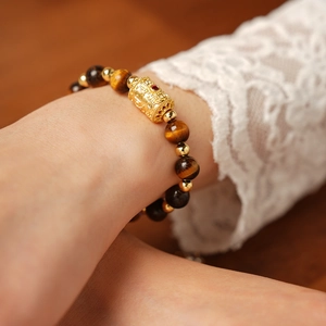 Detailed shot of tiger eye stone bracelet with golden charm bead on a wrist