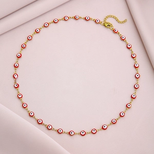 Detailed view of evil eye necklace with red charms and golden lobster clasp on pink fabric