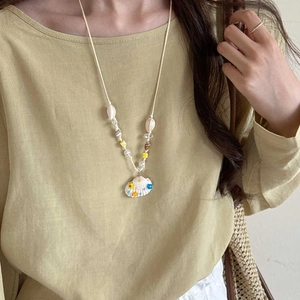 Detail showing shell pendant with floral patterns and pearl beads on woven rope necklace