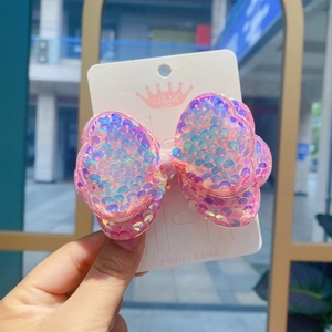 Detail of pink sequin bow hair clip showing multi-color shimmer on white display card