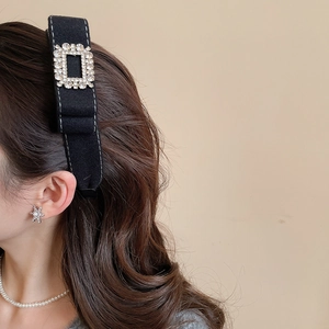 Close-up of a velvet headband with a sparkling rhinestone square buckle worn by a model