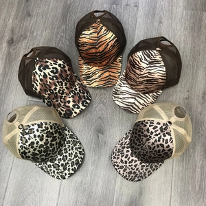 Vijf trucker hats met luipaardprint en ademend mesh op een grijze houten ondergrond