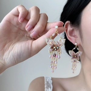 Détail de boucles d'oreilles papillon dorées avec cristaux roses et pampilles élégantes