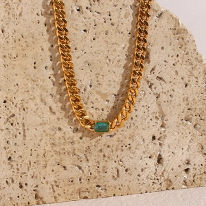 Detail of a 6.5mm gold Cuban chain necklace with a square green zircon on stone background