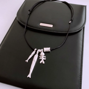Detail of silver fish bone charms on adjustable black cord necklace over a leather clutch