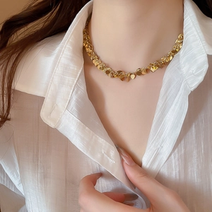 Dettaglio di una collana dorata con nappe a cuore e paillettes indossata da una modella