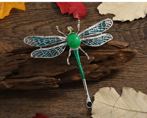 Detailed view of large dragonfly brooch with green enamel wings and gemstones on wood