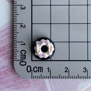 Detailed top view of a 1.2cm black resin donut miniature with pink icing and sprinkles