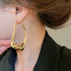 Close-up of a large irregular hollow gold earring worn on a model's ear in detail