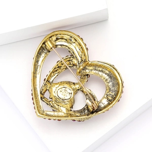 Detailed view of golden heart brooch with red gemstones on a white geometric stand