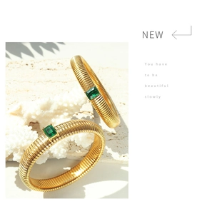 Detail view of gold-plated elastic bracelets featuring textured bands and emerald green stones