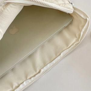 Close-up showing a laptop sliding into a warm white quilted fabric laptop storage bag
