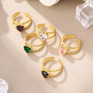 Detail of colorful heart-shaped gemstone rings with twisted gold bands on warm texture