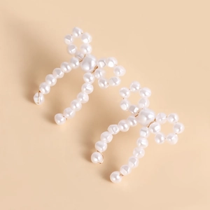Close-up of handmade pearl bow earrings with gold wire and glossy white beads