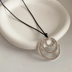 Detail of layered silver geometric pendant necklace with diamonds on a ceramic plate