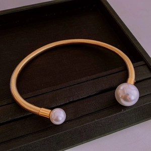 Detail of a golden spiral open cuff bracelet with dual white pearls on black velvet tray
