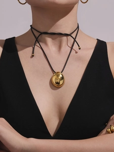 Close-up of a polished golden teardrop pendant on a black cord double-wrap necklace