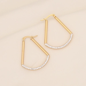 Close-up of geometric gold earrings with micro-paved white zircons on textured fabric