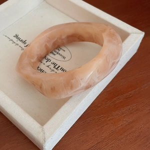 Macro shot of wide pink marble resin bangle on an ivory display tray