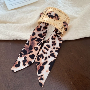 Detail of gold metal cuff with woven texture and leopard print silk ribbon bow tie