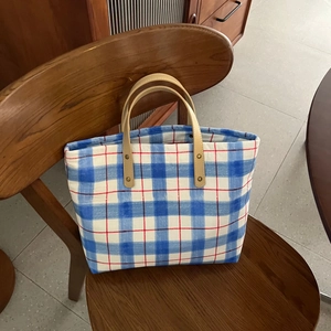 Detail of blue plaid canvas tote with premium brown leather handles on a wooden chair