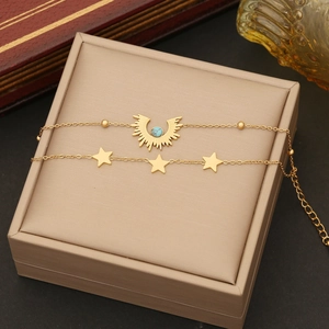 Close-up of double-layer gold bracelet with turquoise eye and star charms on beige box