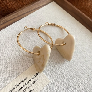 Detail of gold hoop earrings with beige marble texture acrylic heart pendant on wood