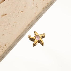 Macro detail of gold-plated starfish pendant with center pink gem on white surface