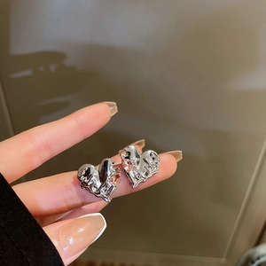 Detail of a silver lava-textured heart earring with a pink teardrop gemstone on fingers