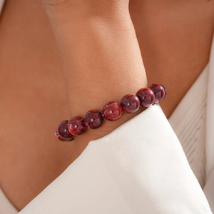 Detailed view of red marble texture beaded bracelet worn on a female wrist in a suit