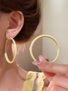 Detail view of large pastel yellow hoop earrings with a matte enamel finish on model