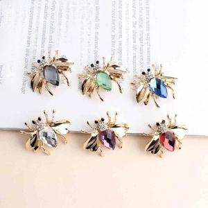 Detail showing six colorful rhinestone bee brooches with crystal wings on a magazine page